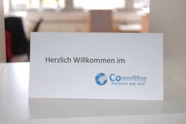 Schild mit "Herzlich Willkommen im Coworking Haltern am See" auf einem Tisch.