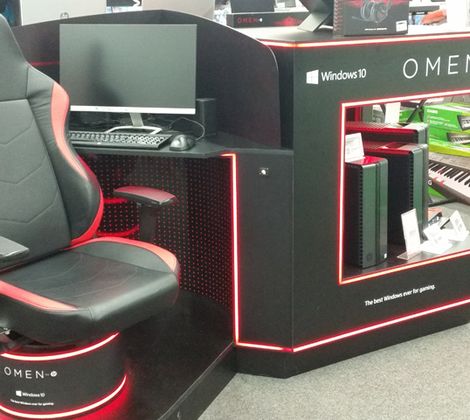 Postazione gaming Omen con sedia, tastiera e monitor in esposizione su pavimento grigio.