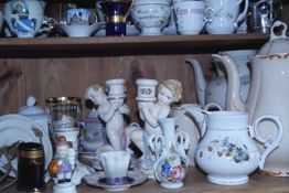 Porzellanfiguren und Geschirr auf einem Regal, mit Engeln und verschnörkelten Mustern verziert.