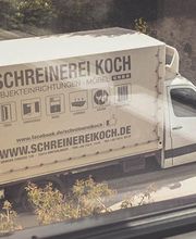 Lieferwagen der Schreinerei Koch parkt auf der Straße, umgeben von Bäumen und Mauern.