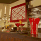 Bar mit Kerzenleuchter, Cocktails und roten Bechern, Holzregal mit Gläsern im Hintergrund.