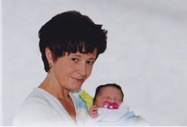 Frau hält ein schlafendes Baby mit Schnuller im Arm, beide lächeln leicht.