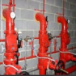 Red industrial pipes with gauges and valves on a brick wall.