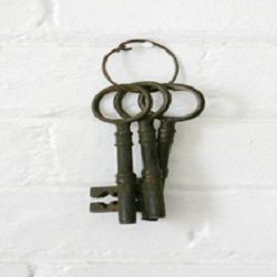 Three antique skeleton keys on a metal ring hanging against a white brick wall.