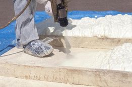 Worker applying spray foam insulation on wooden boards.