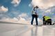 Two workers on a rooftop, wearing safety gear, checking equipment under a blue sky with clouds.