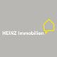 Graues Logo mit weißem Text "HEINZ Immobilien" und gelbem Umriss eines Hauses rechts.