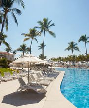 Piscina de hotel rodeada de palmeras y tumbonas bajo un cielo despejado.