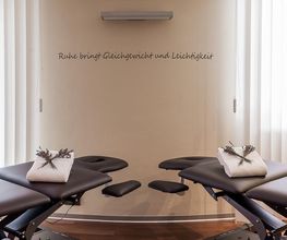 Zwei Massageliegen in modernem Raum mit beruhigender Dekoration und Schriftzug an der Wand.