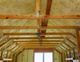 Wooden attic ceiling with exposed beams and insulation installed between the rafters.
