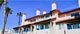 Apartment complex with red roofs, balconies, and palm trees under a clear blue sky.