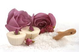 Rosa Rosen, weiße Kerzen und ein Holzlöffel mit Salz auf einem weißen Untergrund.