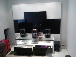 Sala com TV, sistema de som, prateleira, caixas de som e gavetas abertas.