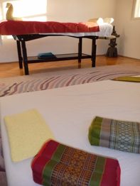 Massageraum mit Liegen, farbigen Tüchern und Teppich auf Holzboden.