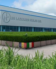 Edificio industriale moderno con logo aziendale esterno, cielo blu e prato in primo piano.