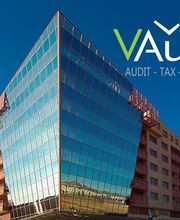 Edificio moderno con fachada de vidrio y logo de VAudit, cielo despejado.