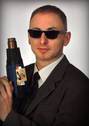 Mann in Anzug und Sonnenbrille hält ein Werkzeug, das wie ein Föhn aussieht.