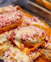 Berinjelas à parmegiana cobertas com queijo derretido e presunto em uma travessa de vidro.