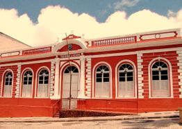 Edifício histórico vermelho e branco com janelas arqueadas e céu azul ao fundo.