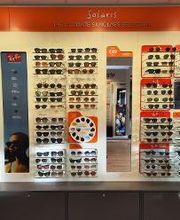 Zonnebrillenwand met diverse modellen in een winkel, tegen een oranje achtergrond.