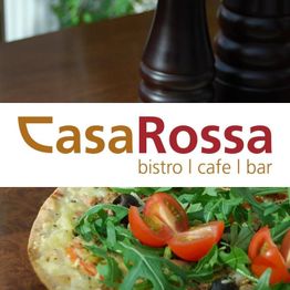 Pizza mit Rucola und Tomaten, Casa Rossa Bistro, Cafe und Bar Logo im Hintergrund.