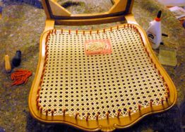 Ein Stuhlsitz wird neu geflochten, umgeben von Werkzeugen und Kleber auf einem Arbeitstisch.