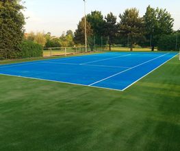 Blauer Tennisplatz im Freien mit grünem Rasen, umgeben von Bäumen bei Tageslicht.