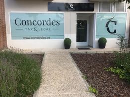 Fachada de la oficina de Concordes Tax & Legal con plantas y camino pavimentado.