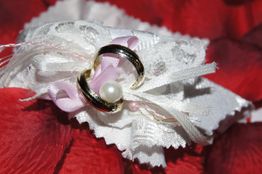 Zwei Goldringe mit weißer Spitze und Perle auf rotem Hintergrund.