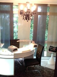 Moderner Nagelstudio-Arbeitsplatz mit schwarzem Kronleuchter und großen Fenstern im Hintergrund.