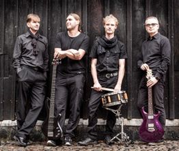 Vier Männer in Schwarz mit Gitarren und Schlagzeug vor Holzwand.