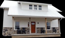 White house with a metal roof, stone accents, and a porch with rocking chairs.