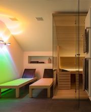 Sala relax moderna con sauna, lettini e illuminazione colorata su parete bianca.