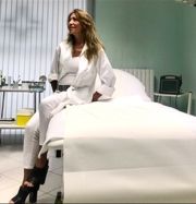 Donna seduta su un lettino medico in una stanza luminosa e sobria, indossa abbigliamento bianco.