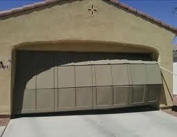 Garage with a partially open, bent door under a clear blue sky.