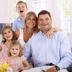 Family portrait with parents and three children smiling in a bright room.