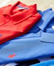 Due polo piegate: una rossa e una blu, con piccoli ricami su un tessuto a righe in sottofondo.