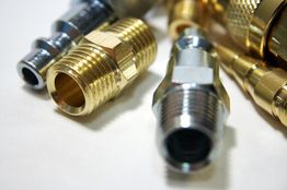 Goldene und silberne Metallverschraubungen nebeneinander auf hellem Hintergrund.