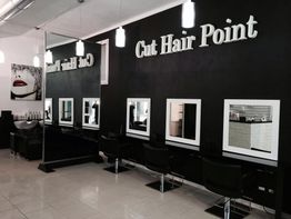 Salone di parrucchiere moderno con specchi e sedie nere, illuminato da lampade bianche pendant.