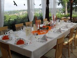 Eleganter Tisch im Restaurant mit weißer Tischdecke, orangen Akzenten und Blick ins Freie.