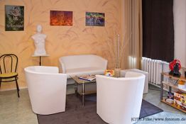 Heller Raum mit weißen Möbeln, Kunst an der Wand und einer roten Kaffeemaschine auf einem Regal.