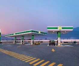 Gasolinera vacía al amanecer con señalización verde y montañas al fondo.