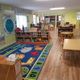 Colorful classroom with a numbered rug, small tables, chairs, and educational decorations.