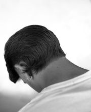 Persona di spalle con capelli corti e orecchino, indossa una maglietta chiara.