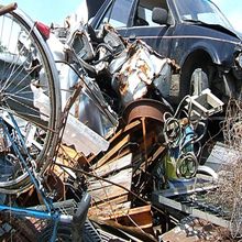 Pile of scrap metal and junk, including a bike wheel and damaged car parts.