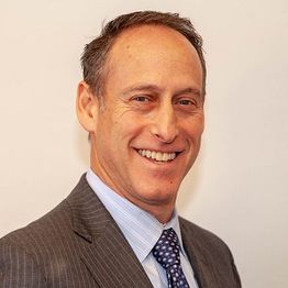 Smiling man in a suit and tie against a plain background.