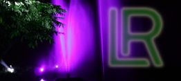 Lila Lichter strahlen nachts neben einem Baum; rechts ein leuchtendes, grünes "LR"-Logo.