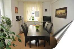 Esszimmer mit langen Tisch, sechs Stühlen, Pflanzen, Wandbildern und einem kleinen Fernseher.
