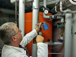 Mann prüft Heizungsanlage mit Manometer in einem Technikraum.