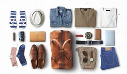 Travel essentials: clothes, shoes, accessories, and a leather bag arranged neatly on a white background.